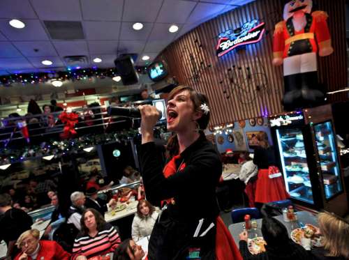 A singer in a festive diner passionately performs with a microphone, surrounded by holiday decorations and diners.
