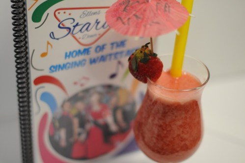 A colorful drink with a straw and umbrella, next to a menu for Ellen's Stardust Diner, featuring musical notes.