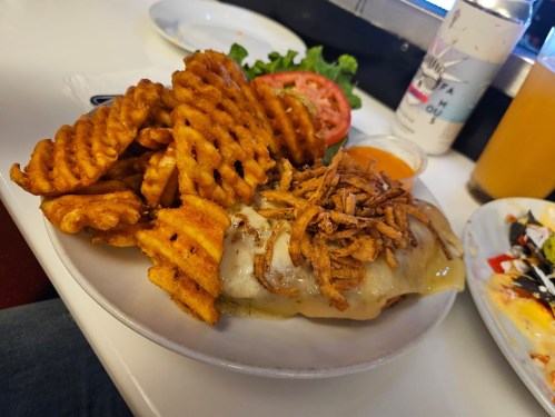 A plate of crispy waffle fries and a sandwich topped with melted cheese and crispy onions, served with a side of sauce.
