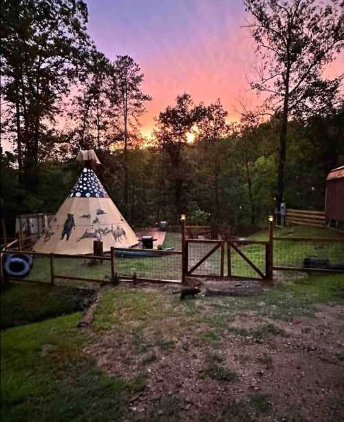 A teepee surrounded by trees at sunset, with a wooden fence and a colorful sky in the background.