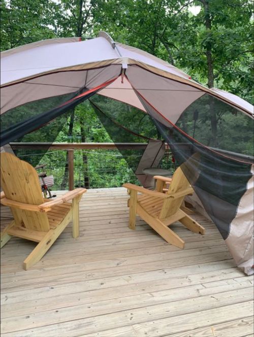 Two wooden chairs on a deck inside a tent, surrounded by trees and greenery.