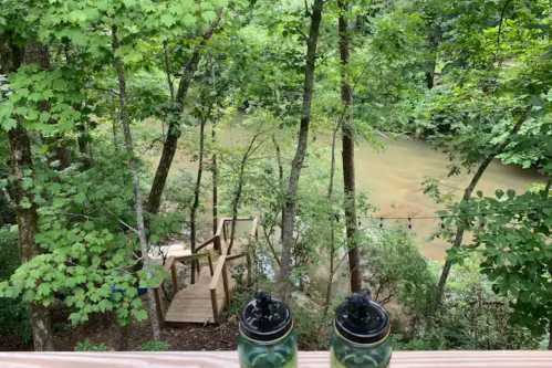 A serene view of a river surrounded by lush greenery, with two cups in the foreground on a wooden railing.