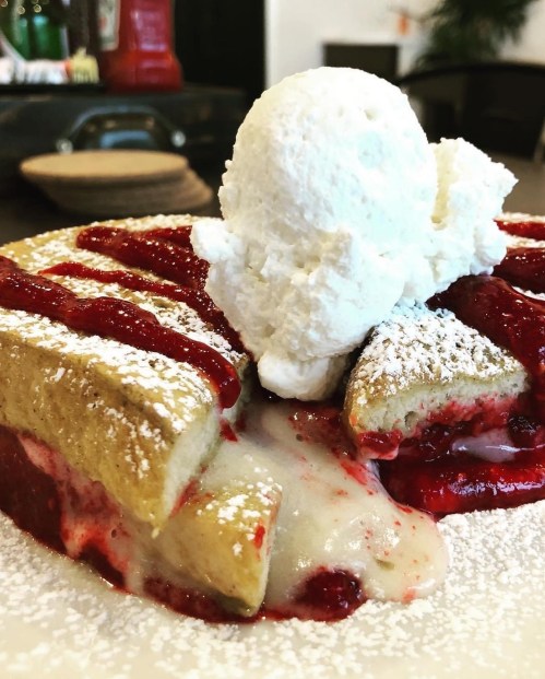 A close-up of a dessert featuring fluffy pancakes filled with strawberry sauce and topped with whipped cream.