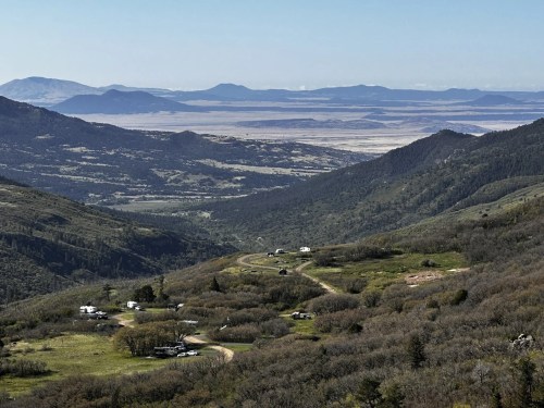 A panoramic view of rolling hills and valleys, with distant mountains and a clear blue sky.