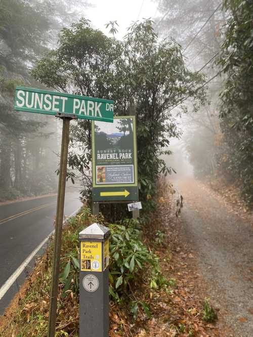 A foggy scene featuring a street sign for Sunset Park Drive and a park information sign near a gravel path.