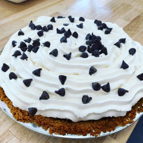 A creamy pie topped with whipped cream and chocolate chips on a graham cracker crust.