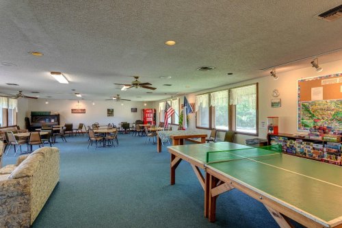 A spacious community room with tables, chairs, a ping pong table, and large windows letting in natural light.