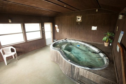A cozy indoor space featuring a wooden hot tub, a white chair, and large windows letting in natural light.