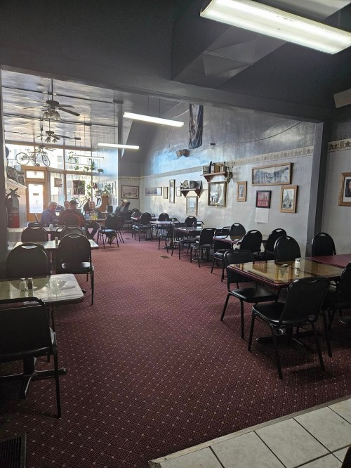 Interior of a cozy restaurant with empty tables, a carpeted floor, and framed pictures on the walls.