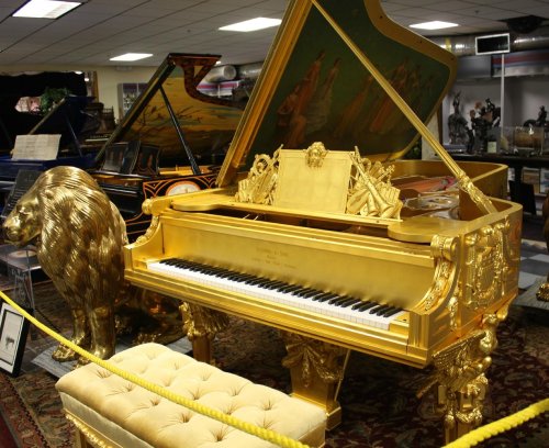 A lavish golden grand piano with ornate details, featuring a lion sculpture, displayed in a music store.