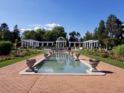 A serene garden with a reflecting pool, surrounded by colorful flowers and elegant white structures under a clear blue sky.