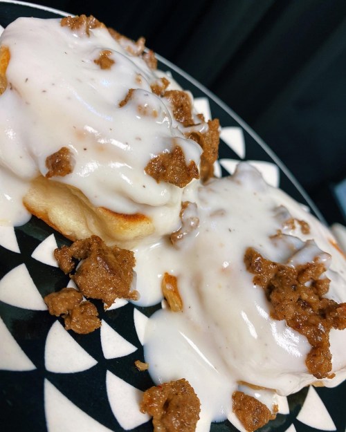 Two fluffy biscuits topped with creamy white icing and crumbled brown topping on a patterned black and white plate.
