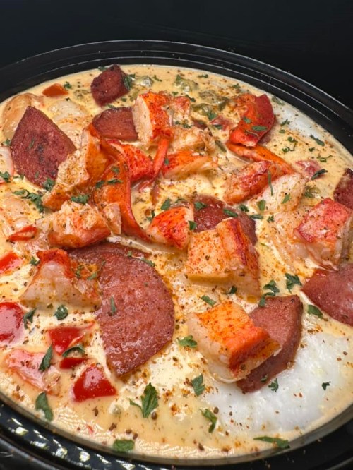 A creamy dish featuring chunks of lobster and sausage, garnished with herbs and spices.