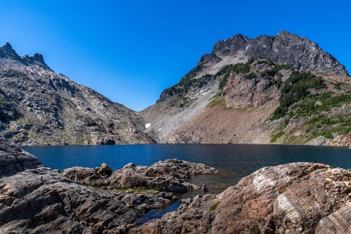 A serene mountain landscape with rocky shores and a clear blue lake under a bright blue sky.