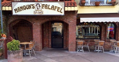 Exterior of Mamoun's Falafel restaurant, featuring a brick facade, outdoor seating, and a sign with the establishment's name.