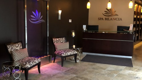 A serene spa reception area with two patterned chairs, a water feature, and a welcoming desk.