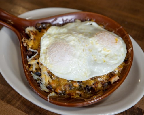 A baked dish with melted cheese, hash browns, and two sunny-side-up eggs in a brown serving dish.