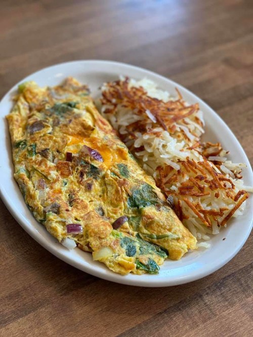 A plate with a vegetable omelet and crispy hash browns on a wooden table.