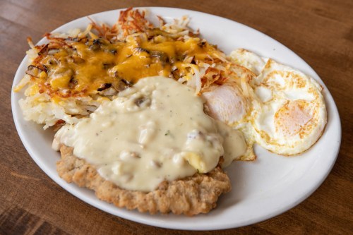 A plate of crispy hash browns topped with melted cheese, fried eggs, and a breaded chicken cutlet smothered in gravy.