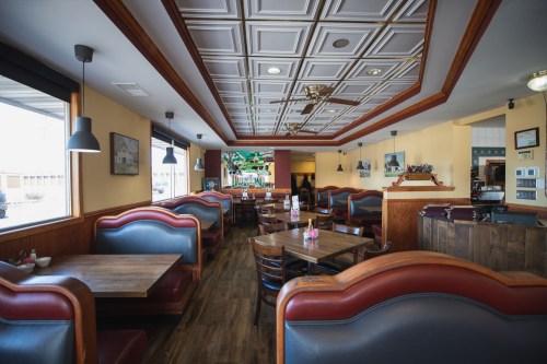Interior of a cozy restaurant featuring wooden tables, leather booths, and decorative ceiling tiles.