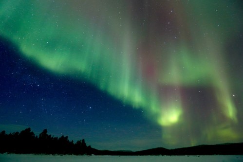 A stunning display of the northern lights illuminates the night sky over a snowy landscape, with stars twinkling above.