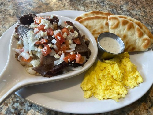 A plate with scrambled eggs, a meat and vegetable mix, and two pieces of flatbread, served with a small sauce cup.