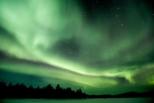 A stunning display of the northern lights illuminates the night sky with vibrant green hues over a snowy landscape.