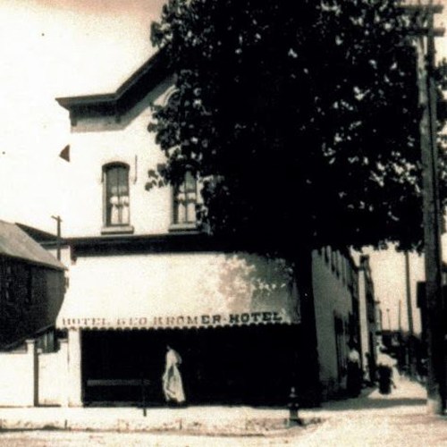 Historic black-and-white photo of the Geo. Bromer Hotel, featuring a woman in front and trees lining the street.