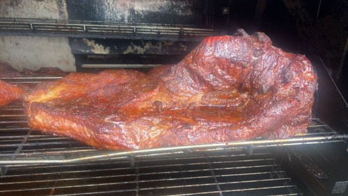 A large, smoked piece of meat resting on a grill rack, showcasing a rich, dark crust and juicy texture.