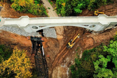 Aerial view of a newly constructed bridge over a construction site, surrounded by trees and heavy machinery.