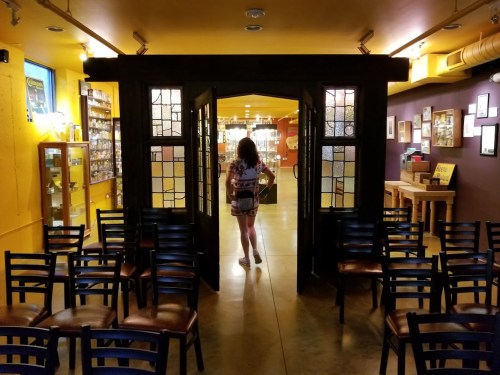 A person walks through a large, open doorway into a colorful room filled with shelves and chairs.