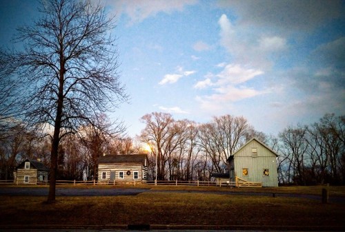 A serene landscape featuring two rustic houses and bare trees under a twilight sky with soft clouds.