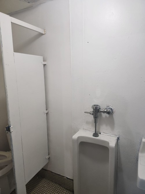 A simple restroom interior featuring a urinal, a toilet stall, and white walls.