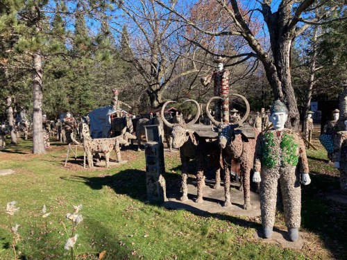 A whimsical outdoor scene featuring stone sculptures of animals and figures among trees in a sunny park.
