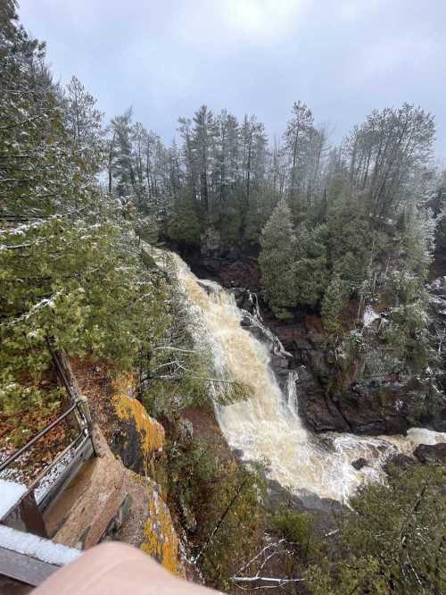 A waterfall cascades down rocky terrain, surrounded by lush green trees and a misty atmosphere.