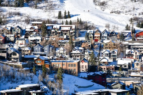 A snowy hillside village with colorful houses and ski slopes in the background. Trees are lightly dusted with snow.