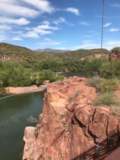 A scenic view of a river winding through lush greenery and rocky cliffs under a blue sky with scattered clouds.