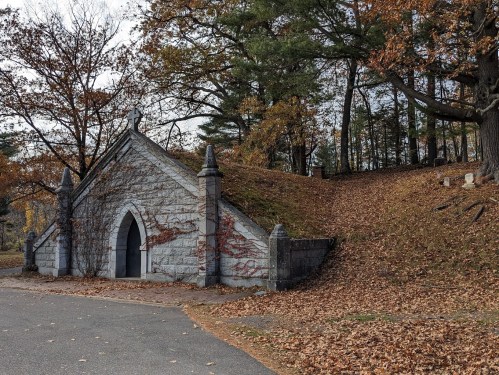 A stone mausoleum surrounded by autumn leaves and trees, with a path leading up to it.