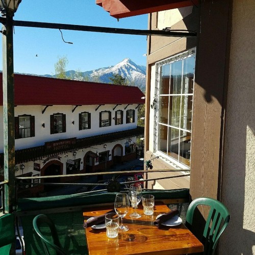 A cozy balcony table set for dining, with a mountain view and charming buildings in the background.