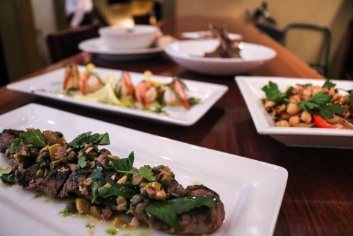A beautifully arranged table featuring gourmet dishes, including grilled meat with herbs and various seafood appetizers.
