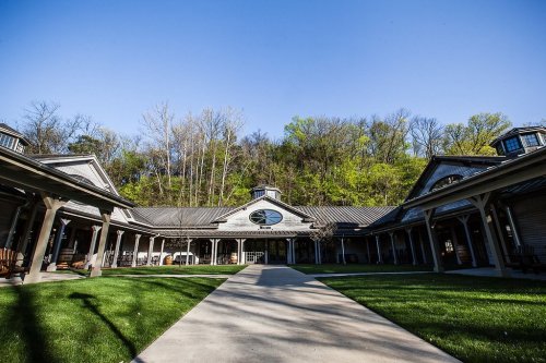 A spacious courtyard surrounded by buildings, with green grass and trees in the background under a clear blue sky.