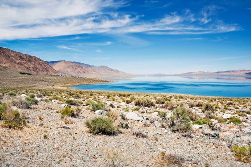 A serene landscape featuring a calm lake surrounded by rocky terrain and mountains under a clear blue sky.