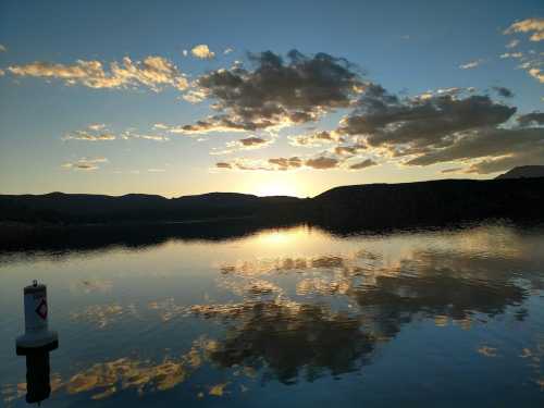 A serene lake at sunset, with clouds reflecting on the water and mountains silhouetted in the background.