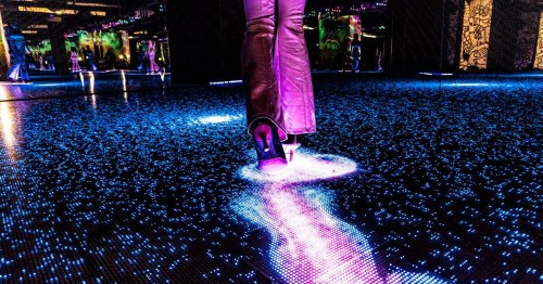 A close-up of a high-heeled shoe stepping on a glowing, illuminated dance floor with colorful lights.