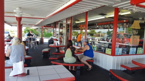 A casual diner with red accents, featuring patrons seated at tables and a view of the open kitchen.