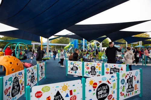 A vibrant playground with colorful equipment, shaded areas, and families enjoying the space on a cloudy day.