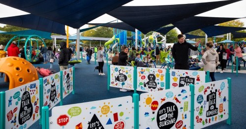 A vibrant playground filled with families, colorful equipment, and banners promoting health and wellness.