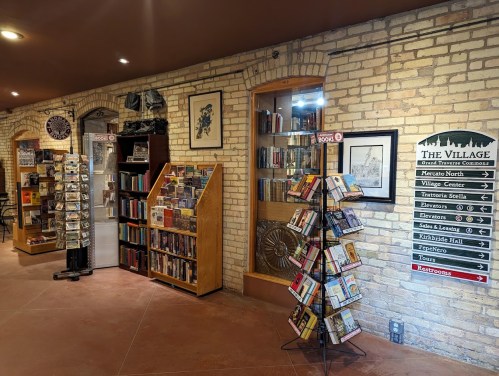 A cozy bookstore interior with brick walls, bookshelves, and a sign for restrooms and directions.