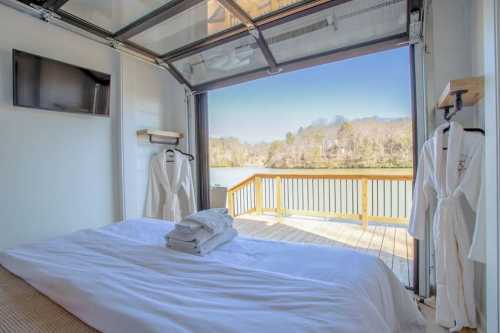 Cozy bedroom with a bed, TV, and open glass doors revealing a scenic view of a lake and trees outside.