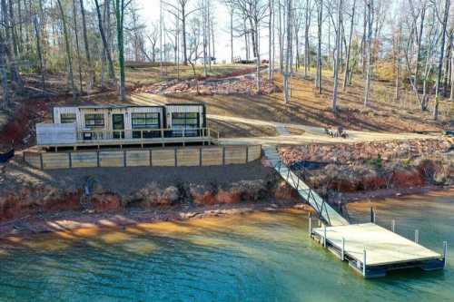 A modern cabin by a lake, surrounded by trees, with a wooden dock extending into the water.